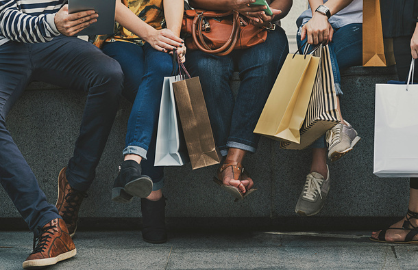 Legs of people sitting while holding bags.