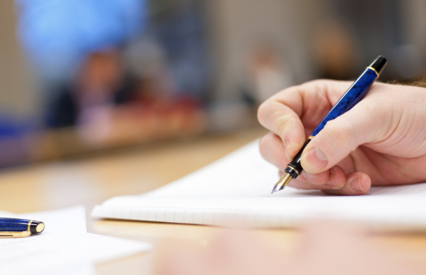 A person holding a pen over a notepad in a meeting