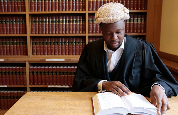 Black male barrister in its wig and gown reading a book.